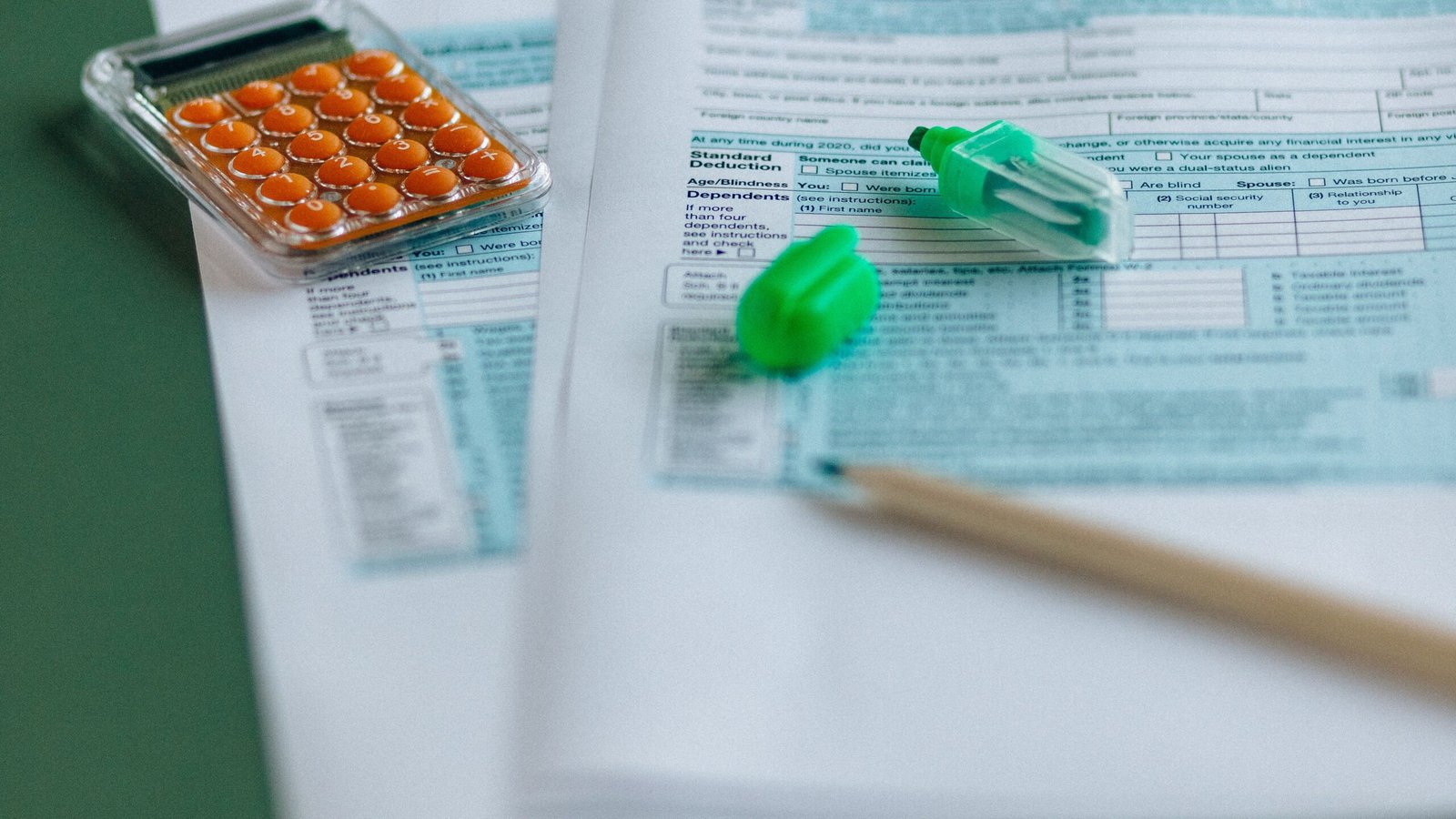 Tax forms and calculator arranged on green desk, illustrating quarterly tax estimation.