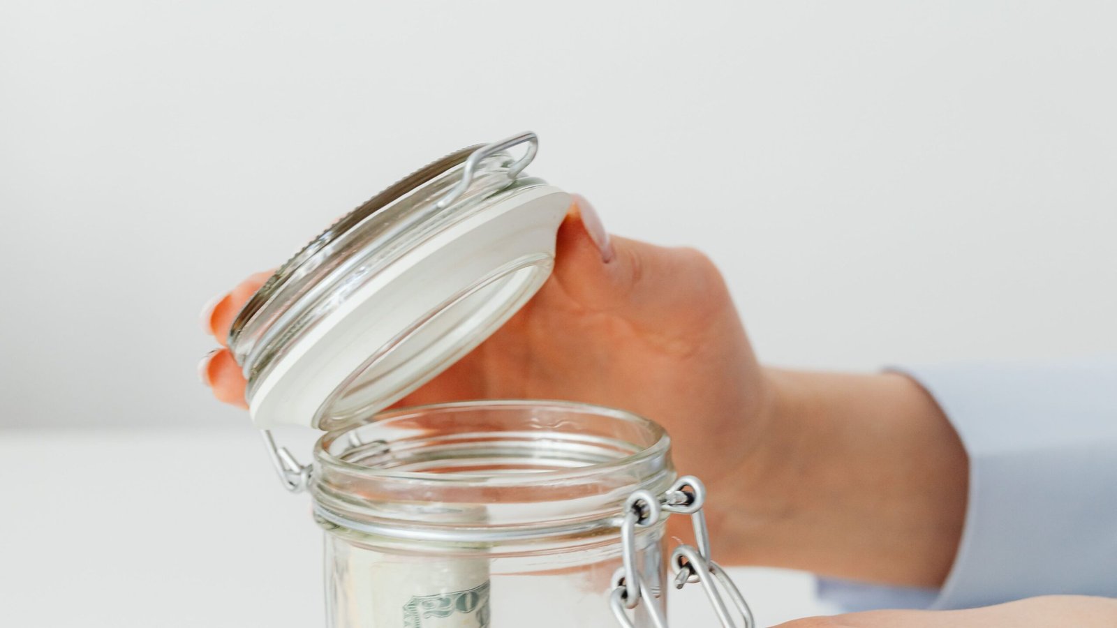 Hands placing cash into a glass savings jar to prepare an emergency fund
