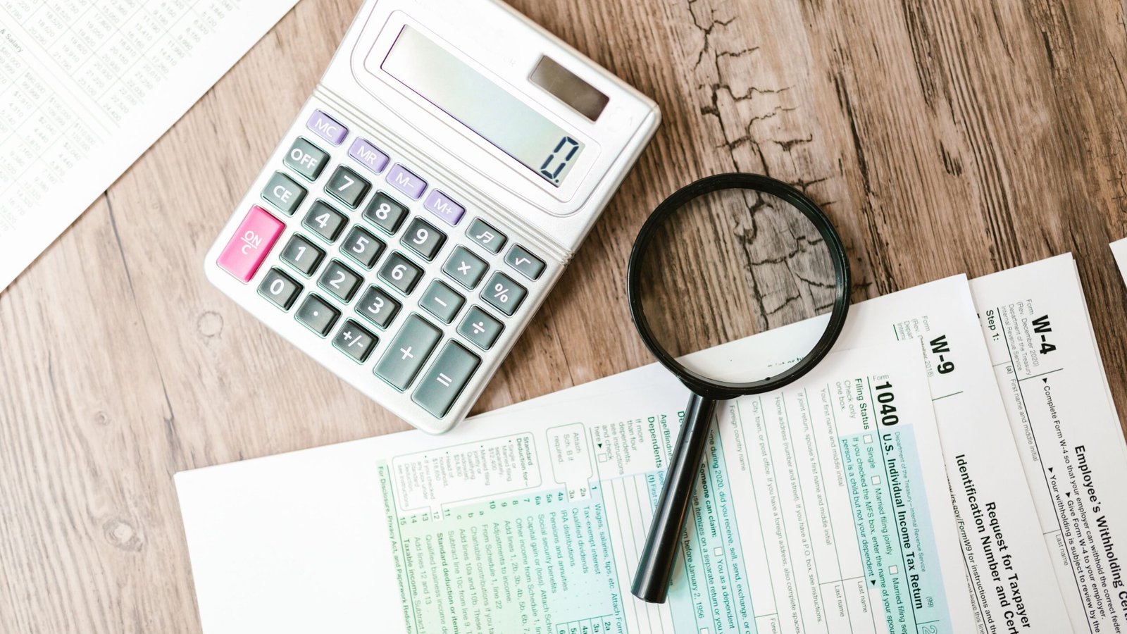 Magnifying glass and calculator beside tax documents for identifying bookkeeping mistakes.