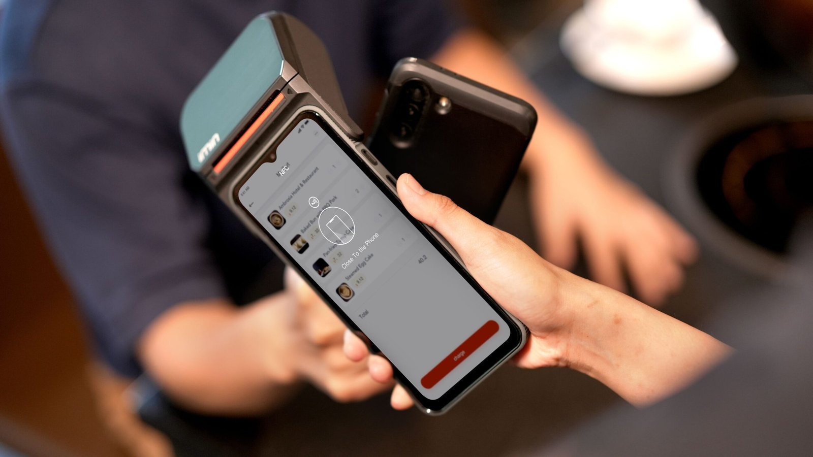 A customer holds a smartphone beside a contactless payment terminal.