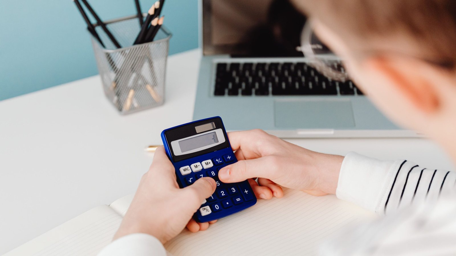 Hands using a calculator at a workspace for budgeting freelance business expenses