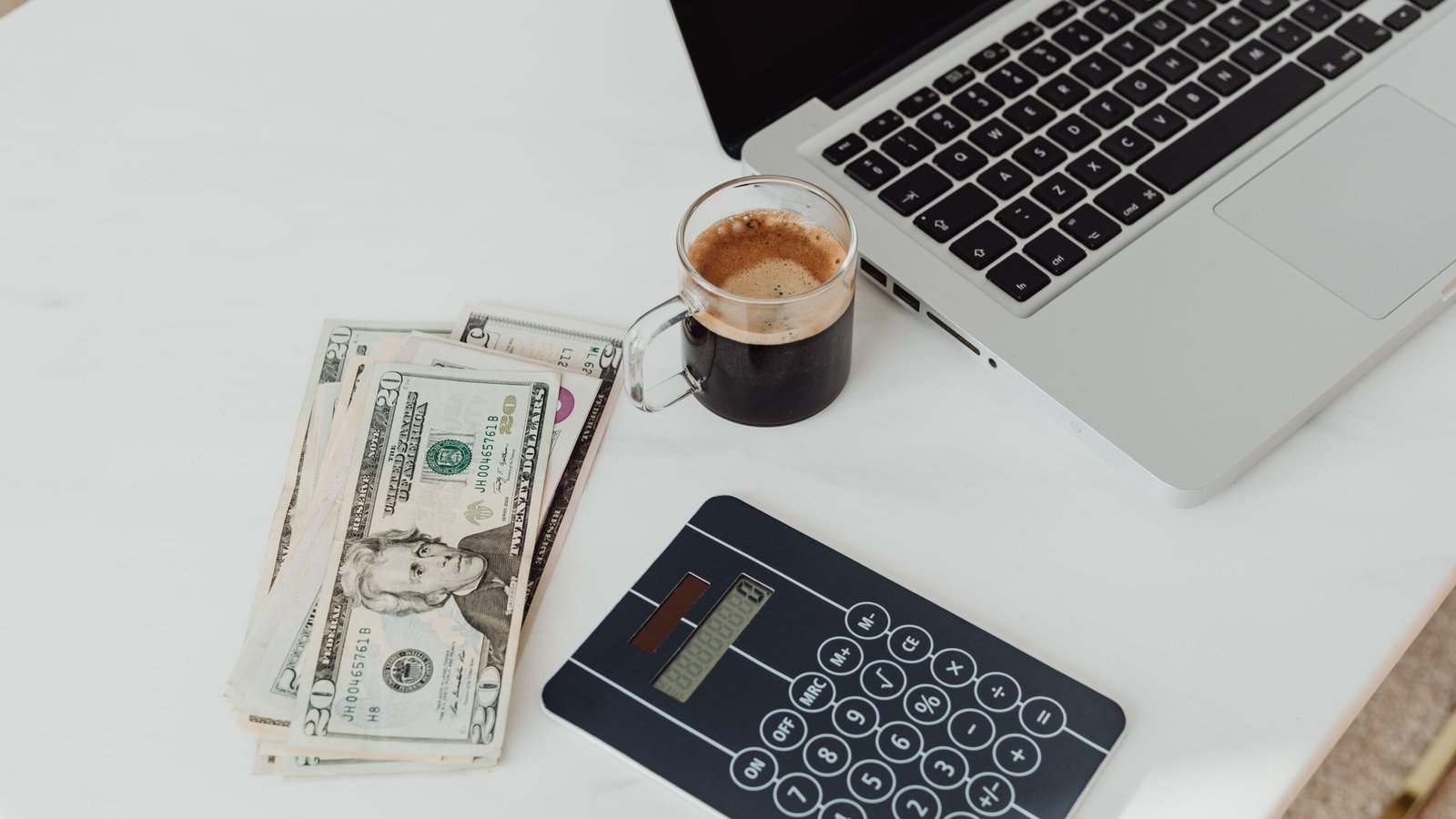 Calculator, laptop, coffee and U.S. dollar bills arranged on a desk for freelance income planning