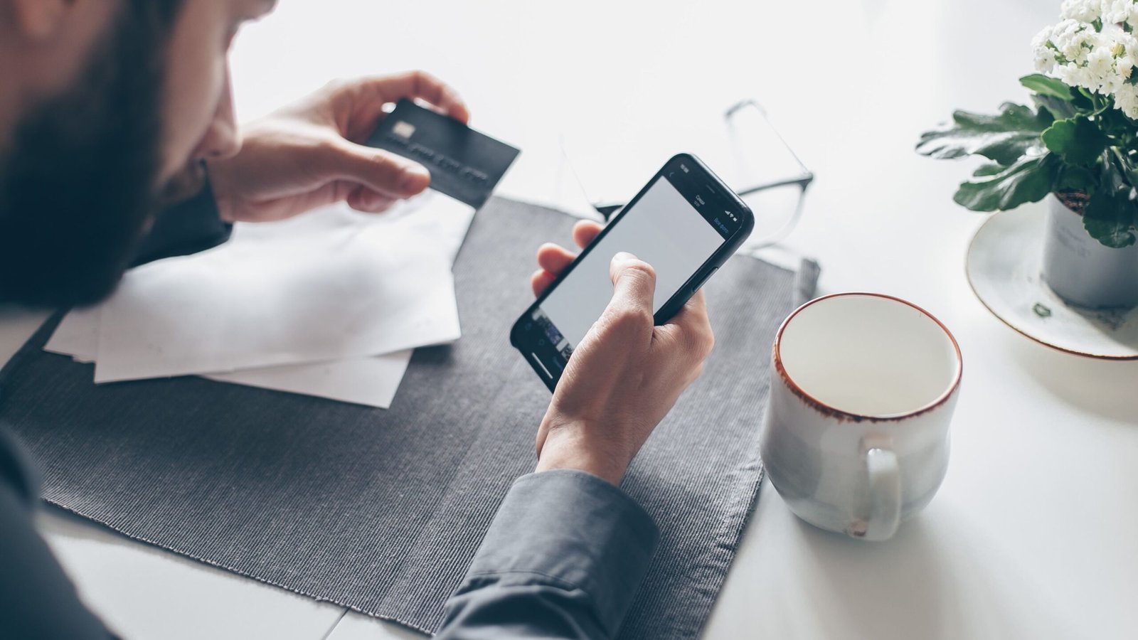 A person reviews a smartphone while holding a payment card at a table.