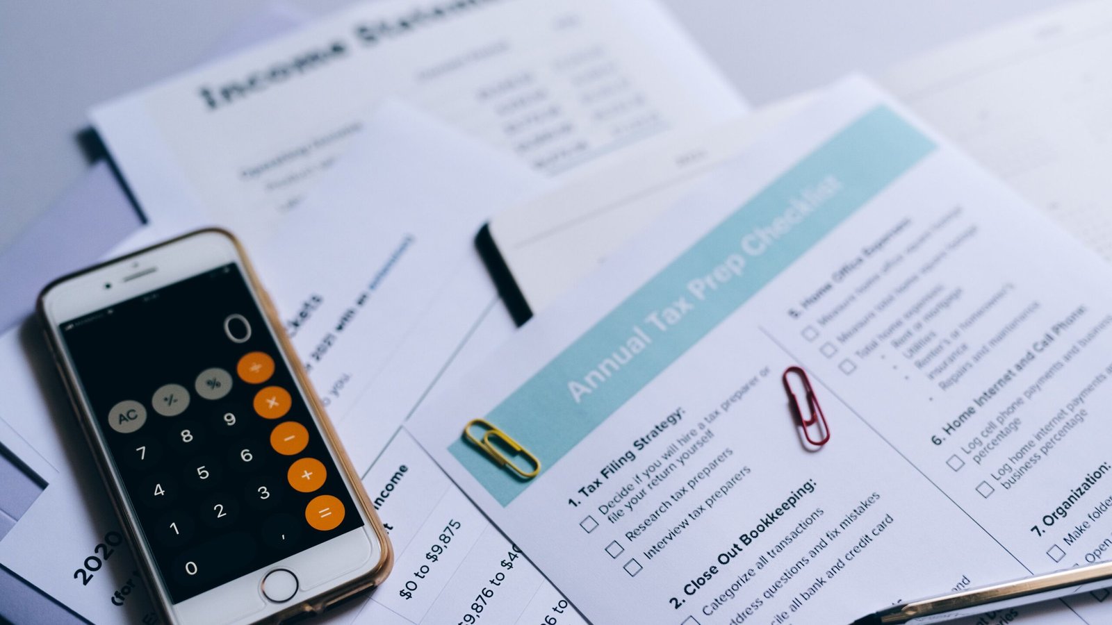 Smartphone calculator and financial records arranged for monthly self-employed bookkeeping.
