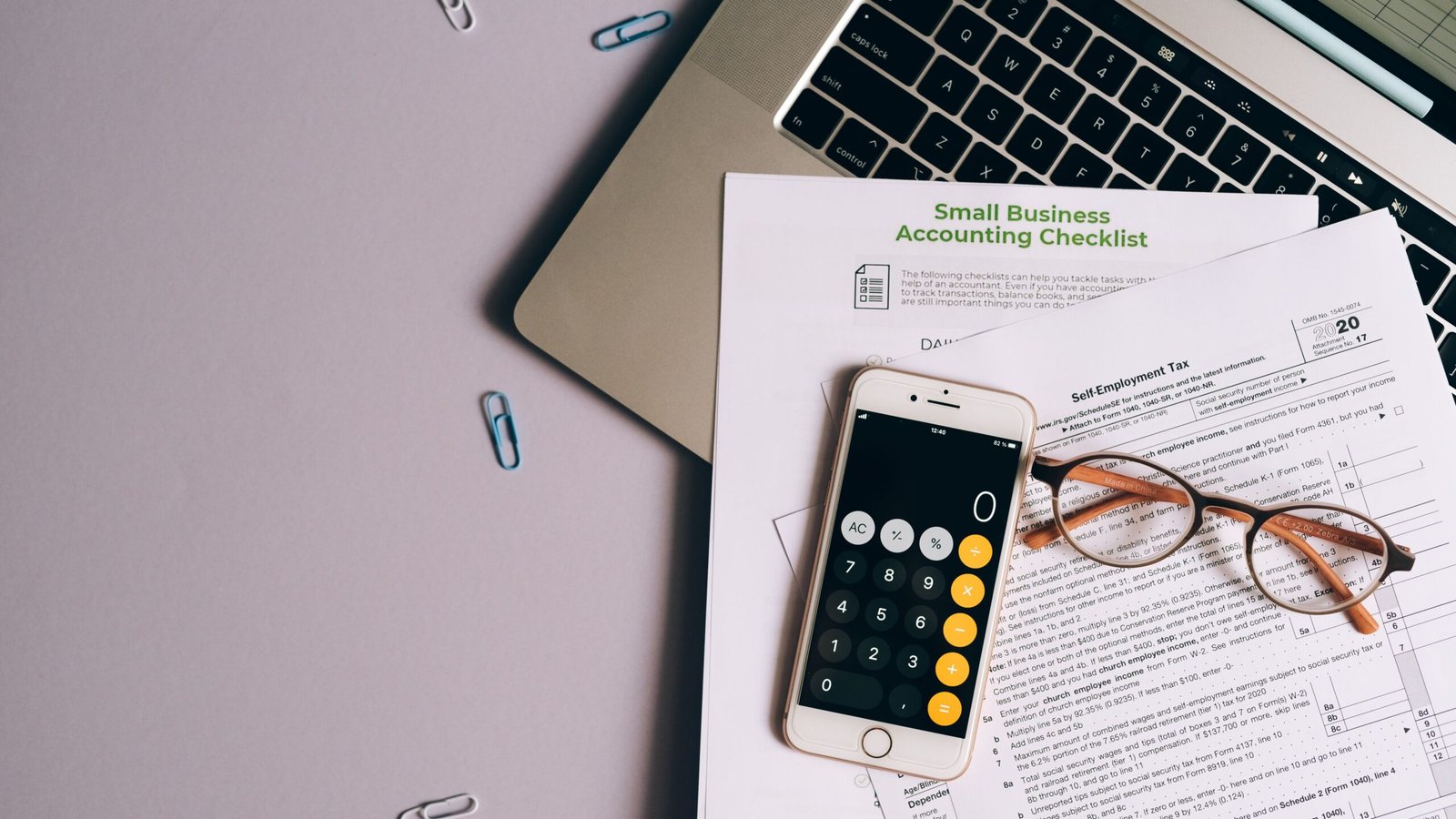 Smartphone, glasses and finance papers beside a laptop for planning taxes during slow income months