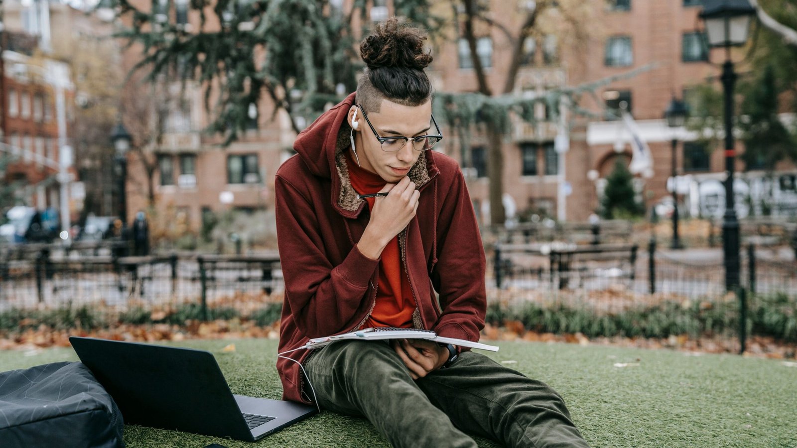 College student working on a laptop with a notebook outside on campus