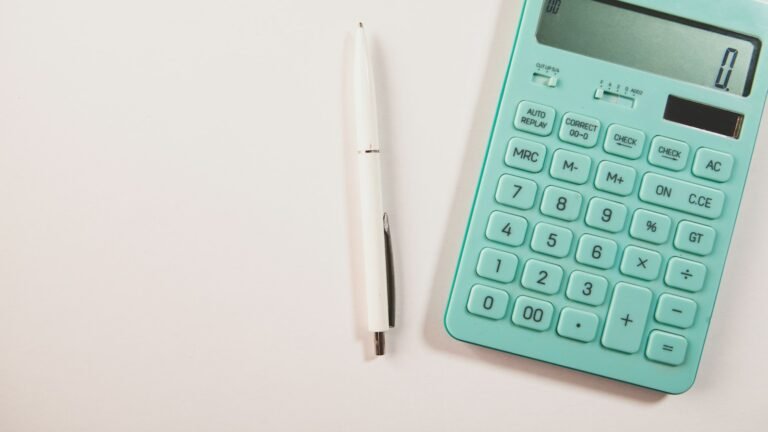 Teal calculator and white pen on a light desk.