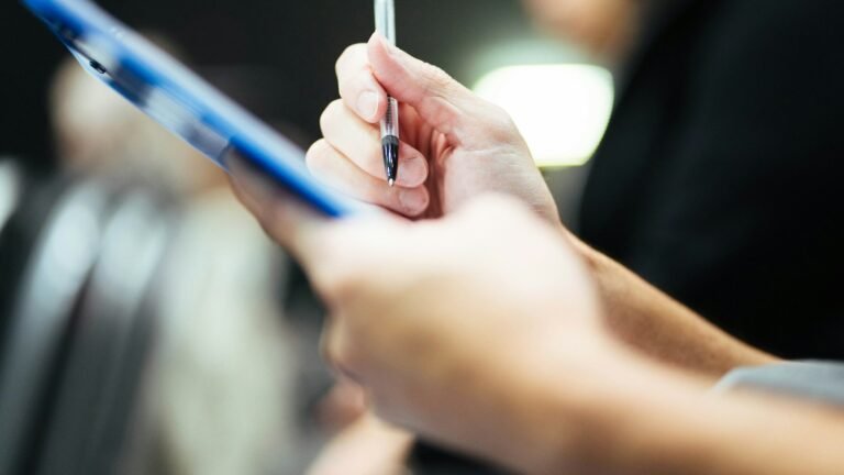 Close-up of hands holding a pen and blue clipboard.
