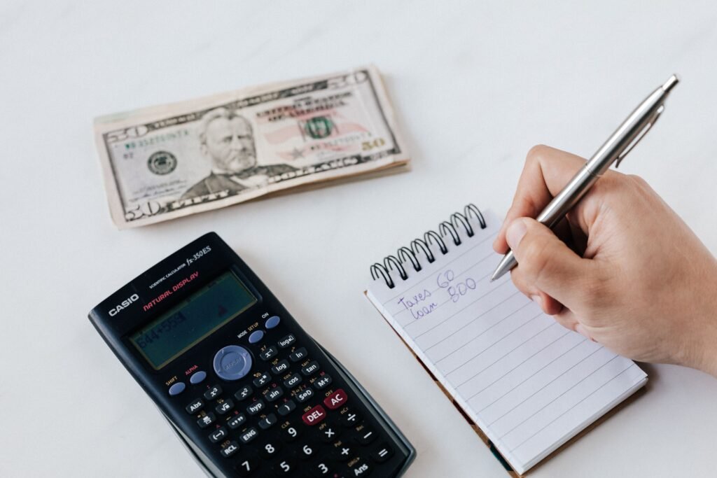 Person writing a financial budget beside a calculator and dollar bills