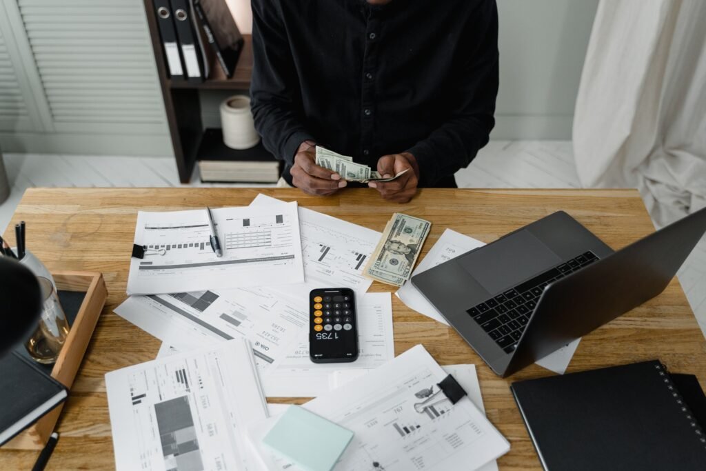 Person counting dollar bills beside loan documents and a calculator