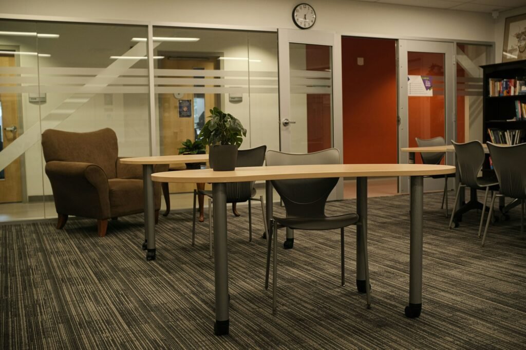 Empty tables and chairs in a study room, with a potted plant on a table.