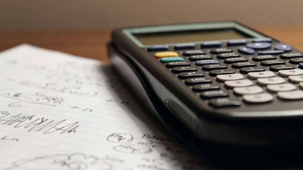 A scientific calculator rests on lined paper with handwritten mathematical notes.