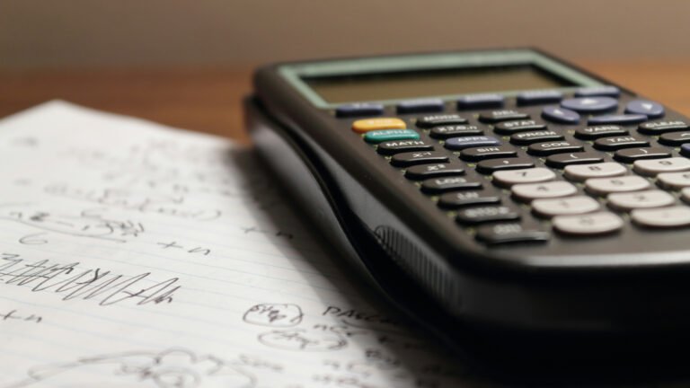 A scientific calculator rests on lined paper with handwritten mathematical notes.