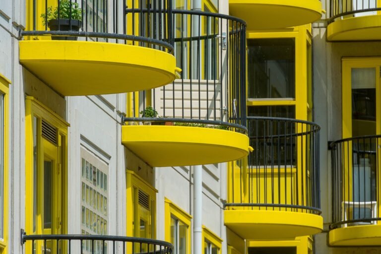 Curved yellow balconies with black railings and potted plants on a light-colored building.
