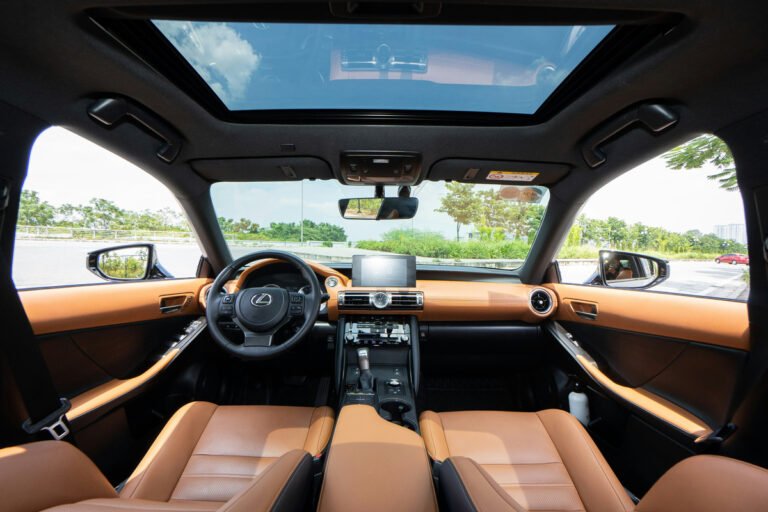 A car cabin has tan front seats, a steering wheel, a central display and a glass roof.