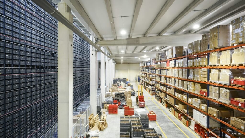 Warehouse shelves holding cartons and storage bins beside an open aisle.