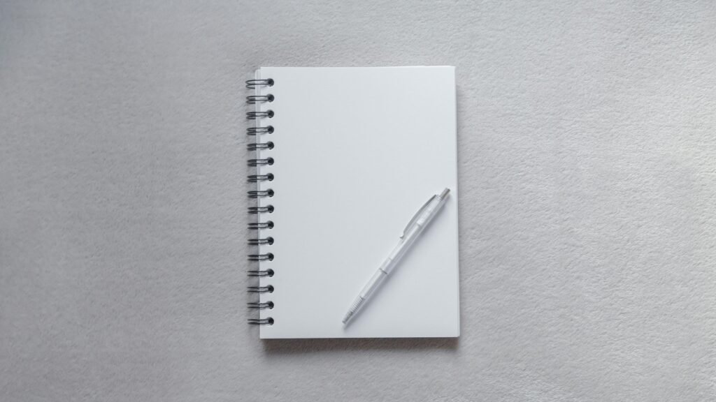 Blank spiral notebook and a white pen on a gray surface.