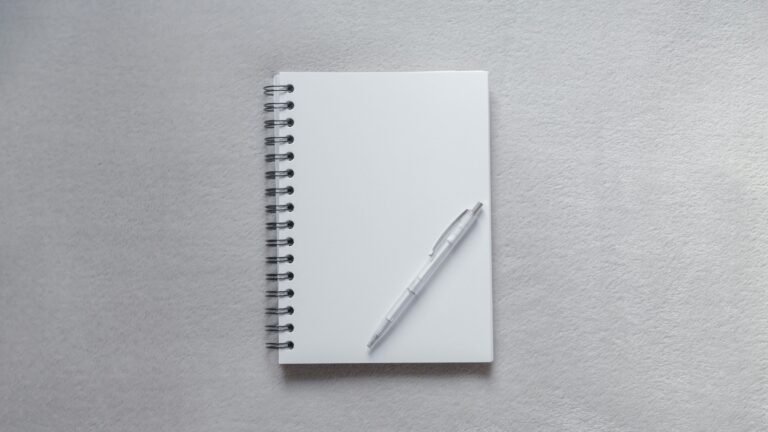 Blank spiral notebook and a white pen on a gray surface.