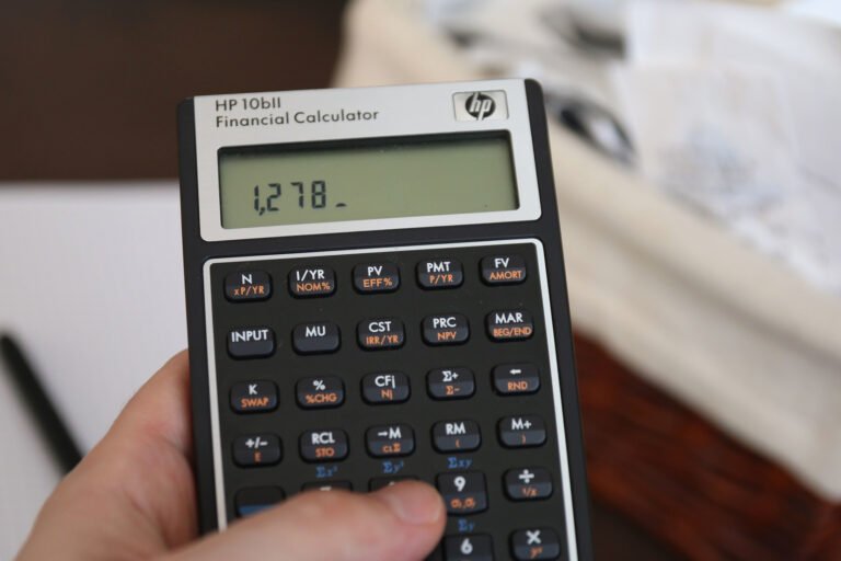 A hand holding a black financial calculator beside a desk.