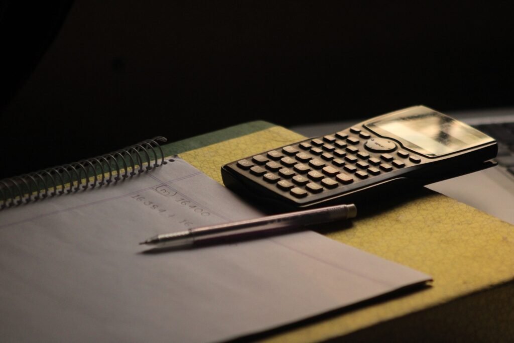 A black calculator and pencil rest on an open spiral notebook.