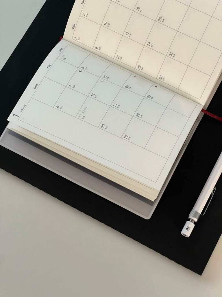 An open monthly planner rests on a dark desk mat beside a mechanical pencil.
