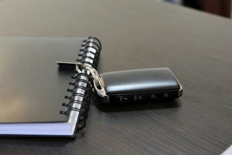 Unbranded car key fob beside a closed spiral notebook on a desk.