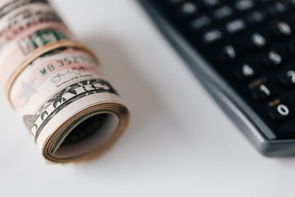 A roll of U.S. dollar bills lies beside black calculator keys.