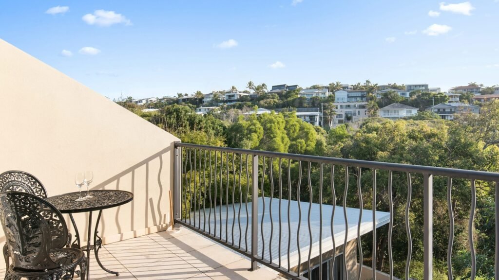 A furnished balcony overlooking trees and neighboring houses.
