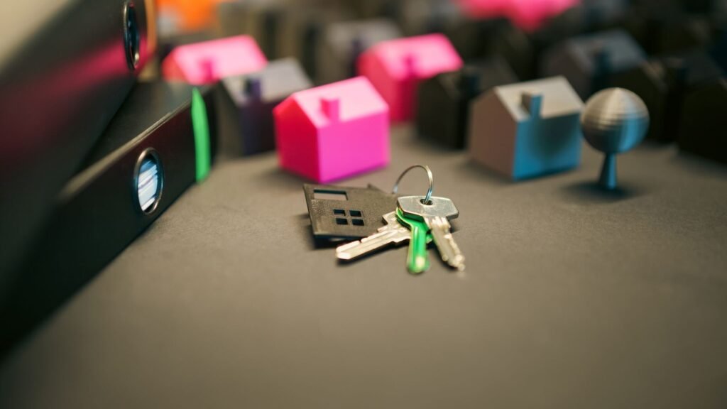 Keys and a house-shaped keychain on a desk beside small colorful model houses.