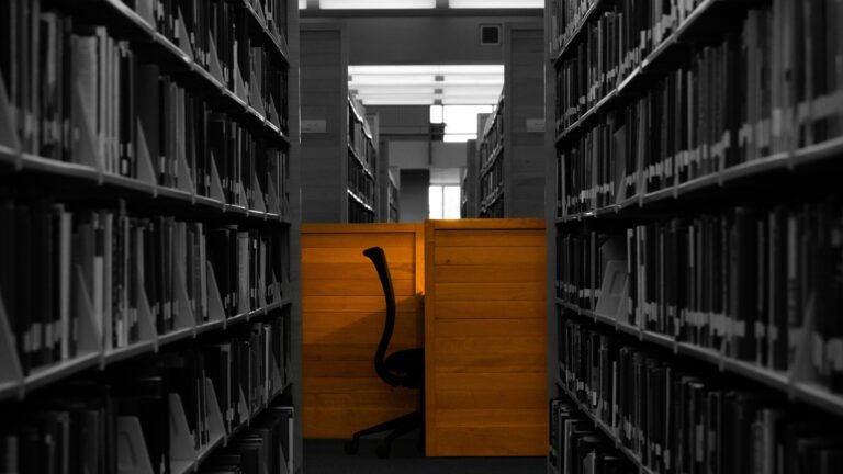 An empty study cubicle at the end of an aisle between library bookshelves.