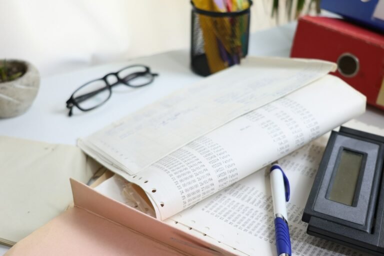 Financial paperwork in a folder with a calculator, pen and reading glasses on a desk.