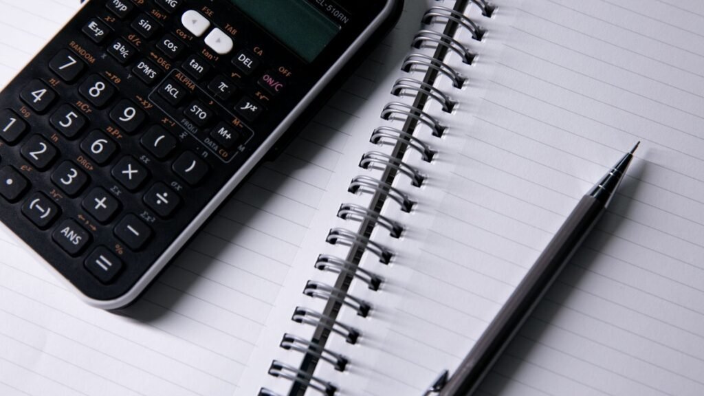 Calculator, pen and blank lined notebook on a desk.