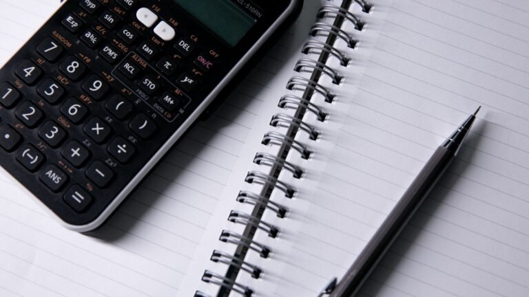 Calculator, pen and blank lined notebook on a desk.