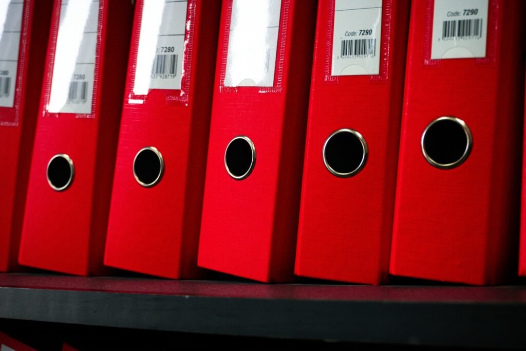 Red document binders stand in a row on a dark shelf.
