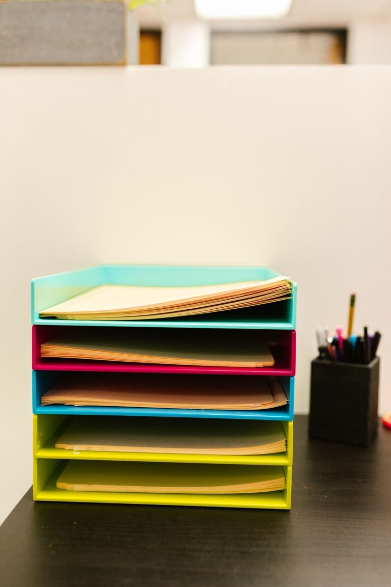 Manila folders in five colorful document trays beside a pen holder on a desk.