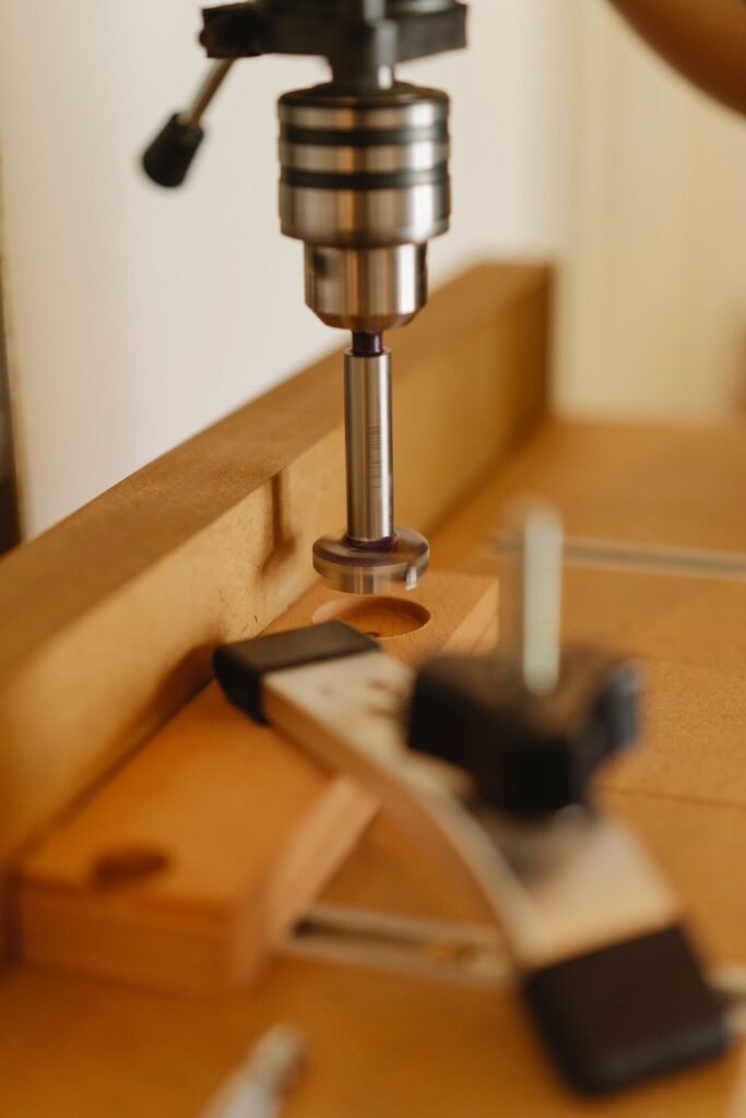 Drill press above a wooden workpiece held by a clamp.