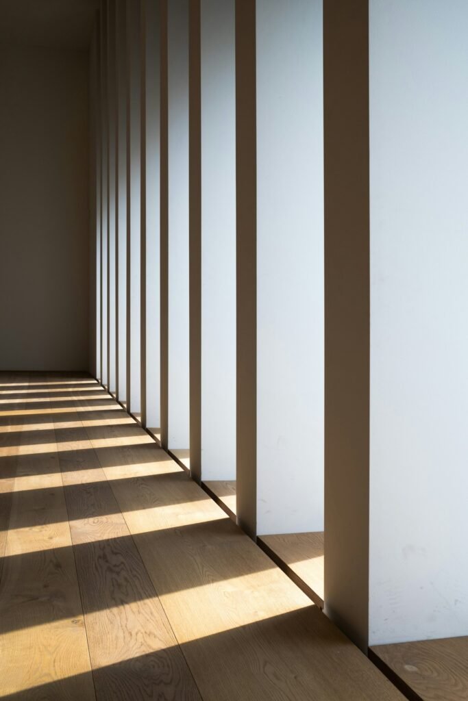 Sunlight falls across a wooden floor beside a row of white interior columns.