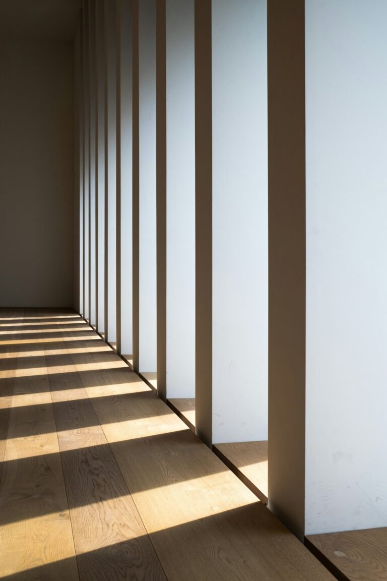 Sunlight falls across a wooden floor beside a row of white interior columns.