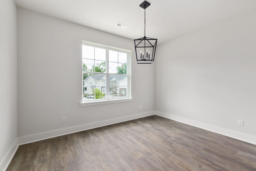 Unfurnished room with pale walls, wood-look flooring, a window and a black pendant light.