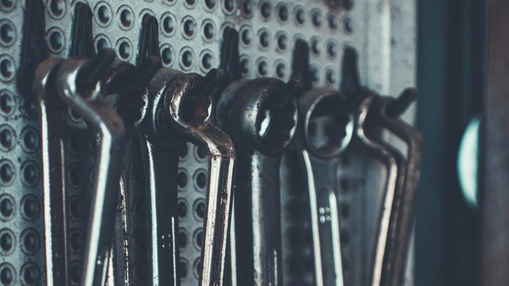 Metal combination wrenches hanging from a perforated workshop tool board.