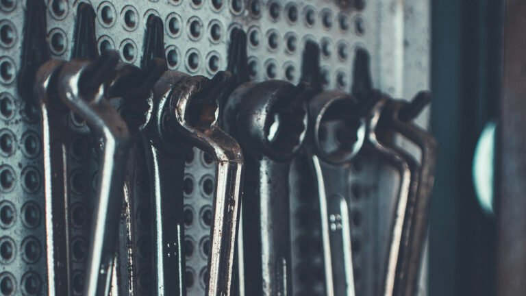 Metal combination wrenches hanging from a perforated workshop tool board.