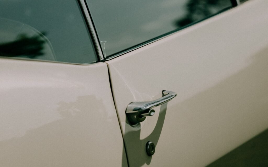 A chrome handle and lock on a white car door beneath a dark window.