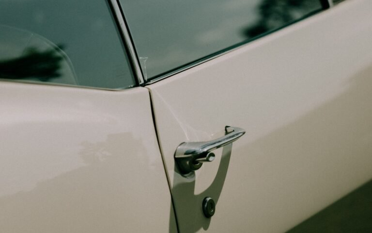 A chrome handle and lock on a white car door beneath a dark window.