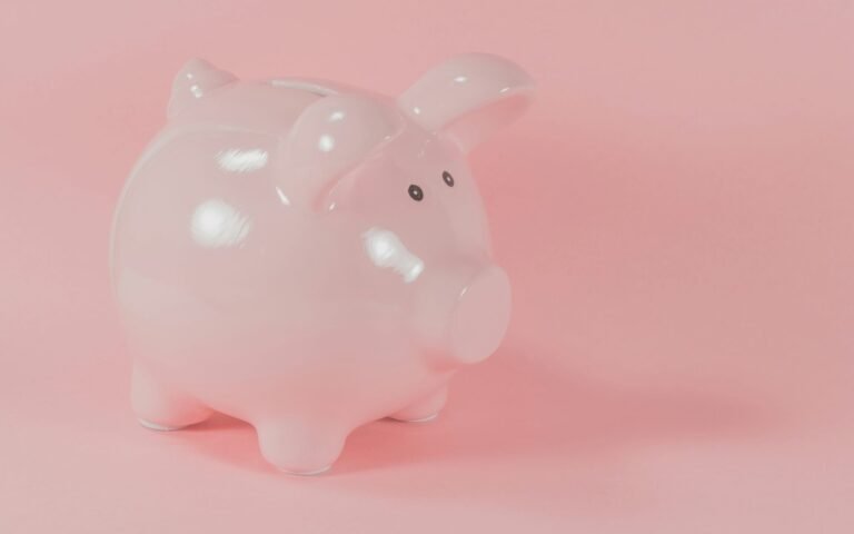 A pink ceramic piggy bank on a pink surface and background.