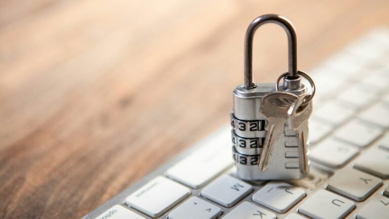 Combination padlock and keys resting on a white computer keyboard.
