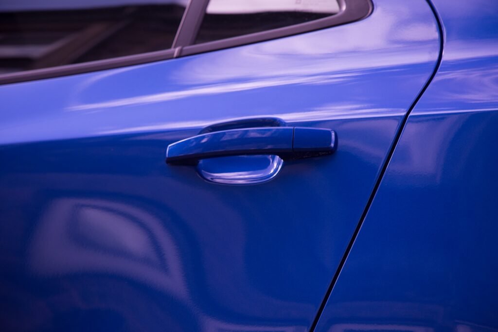 Close-up of a handle on a blue car door beneath the window.