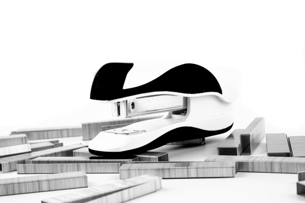 A black-and-white stapler surrounded by strips of metal staples on a white surface.