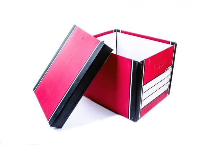 An empty red cardboard storage box with its lid leaning beside it.