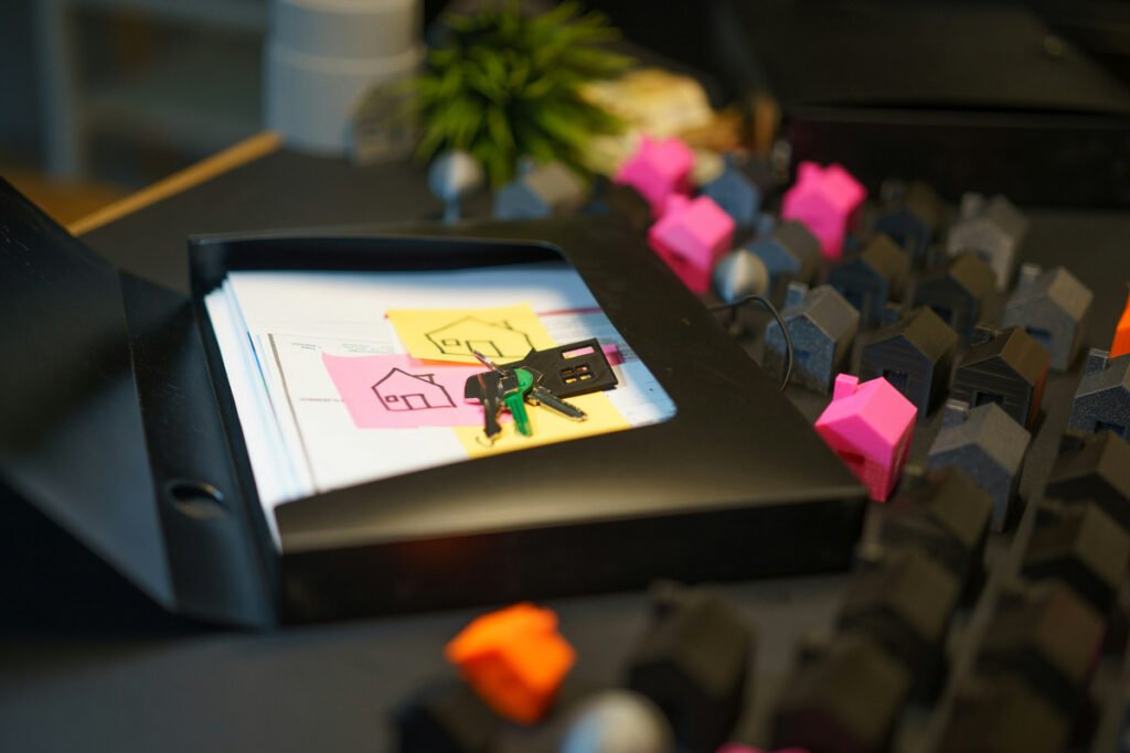 Keys and house sketches rest on paperwork in an open folder beside miniature houses.