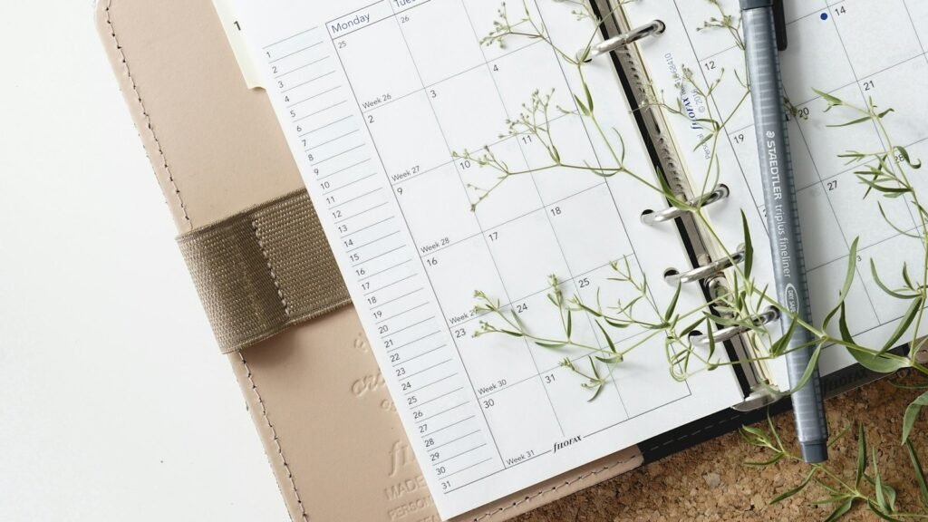 Open paper planner with a pen and green sprigs on the pages.
